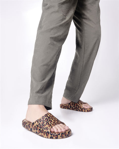 Model's legs in grey pants wearing a pair of beige Free Print Slides with leopard print