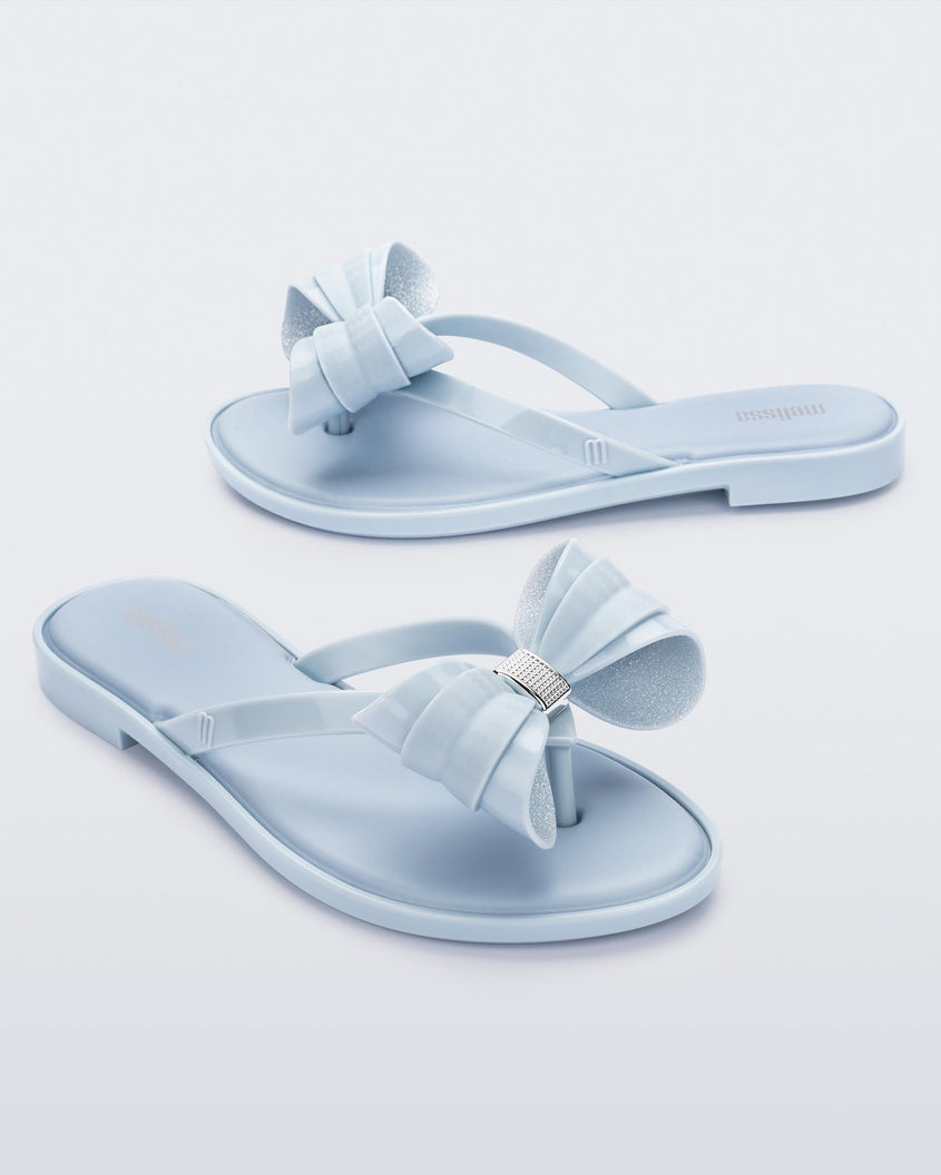 Angled view of a pair of Melissa slim strap flip flops in glitter blue with bow applique