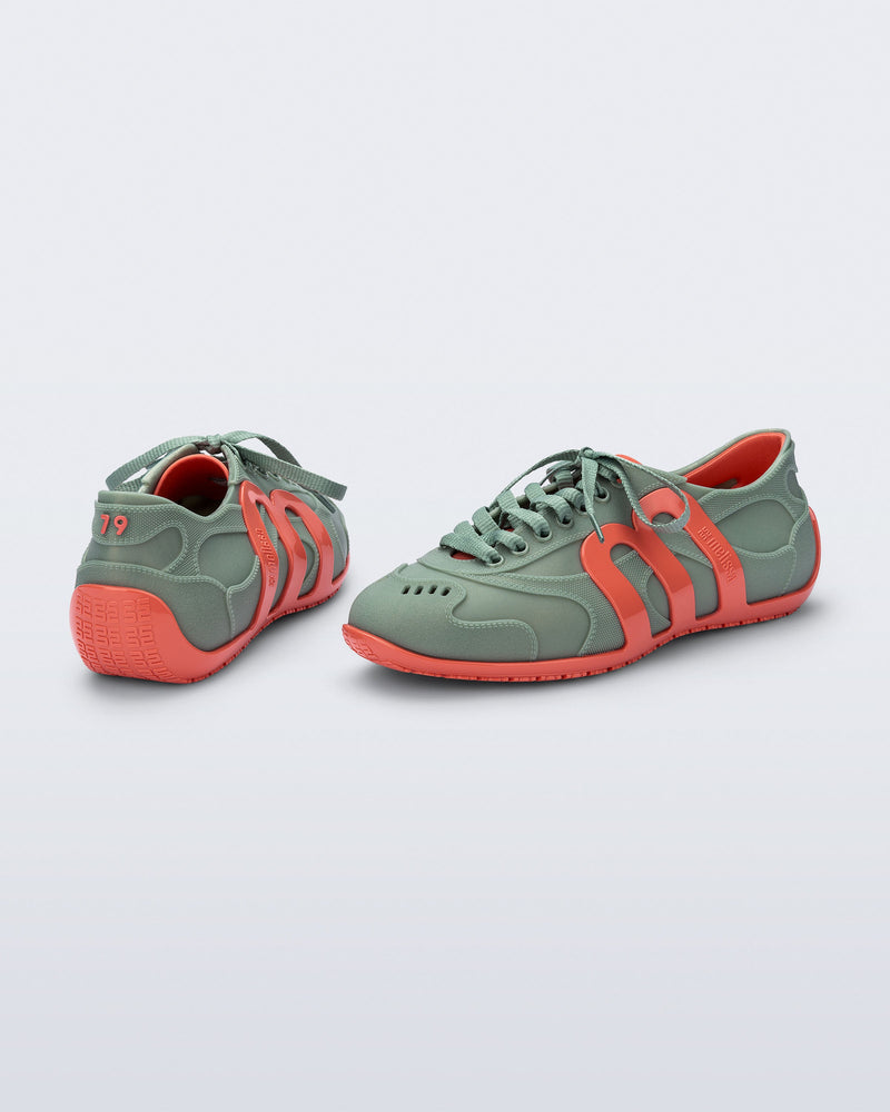 Back and side view of a pair of green Motion sneakers with orange colored sole and M monogram on side and 79 on heel