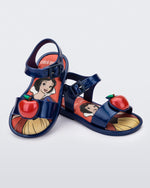 An angled top and side view of a pair of metallic blue Mini Melissa Mar Sandal Princess sandals, leaning on eachother, with an apple detail on the front strap, an ankle strap and Princess Snow White soul