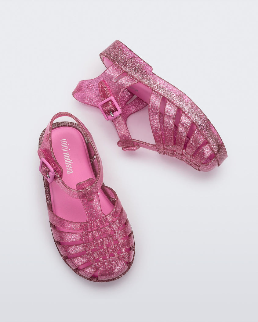 Top and side view of a pair of Mini Melissa Possession baby sandals in glitter pink with velcro buckle closure on the ankle straps