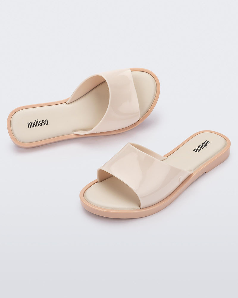 An angled side and top view of a pair of beige tortoiseshell Melissa Miranda slides
