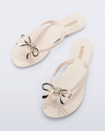 Top view of a pair of beige Harmonic Iris flip flops with gold bow