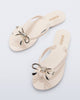 Top view of a pair of beige Harmonic Iris flip flops with gold bow