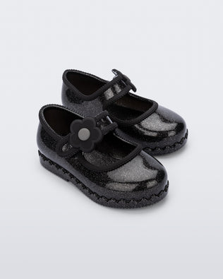 Side view of a pair of black Hip Ballerina baby flats with strap with flower