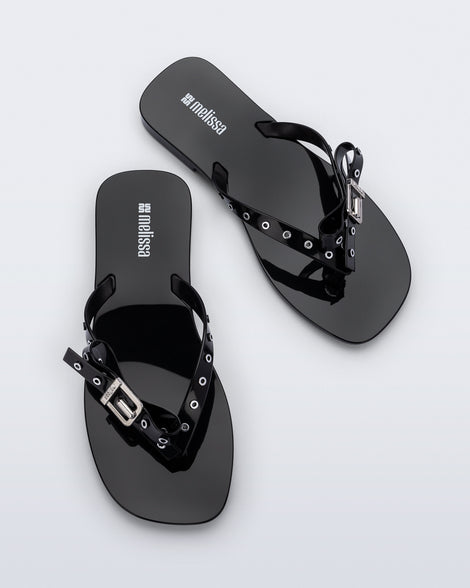 Top view of a pair of black Harmonic Squared flip flops with bow on strap