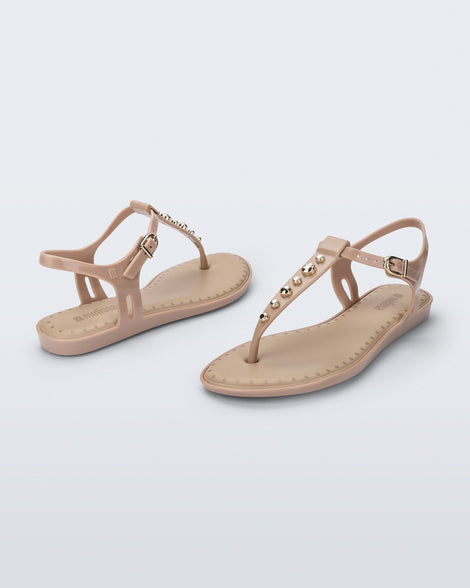 Angled view of a pair of beige Solar Boho t-strap sandals with ,metallic detailing on the front strap