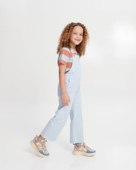Child model in blue overalls wearing a pair of blue X Beat kids sneakers with beige trim