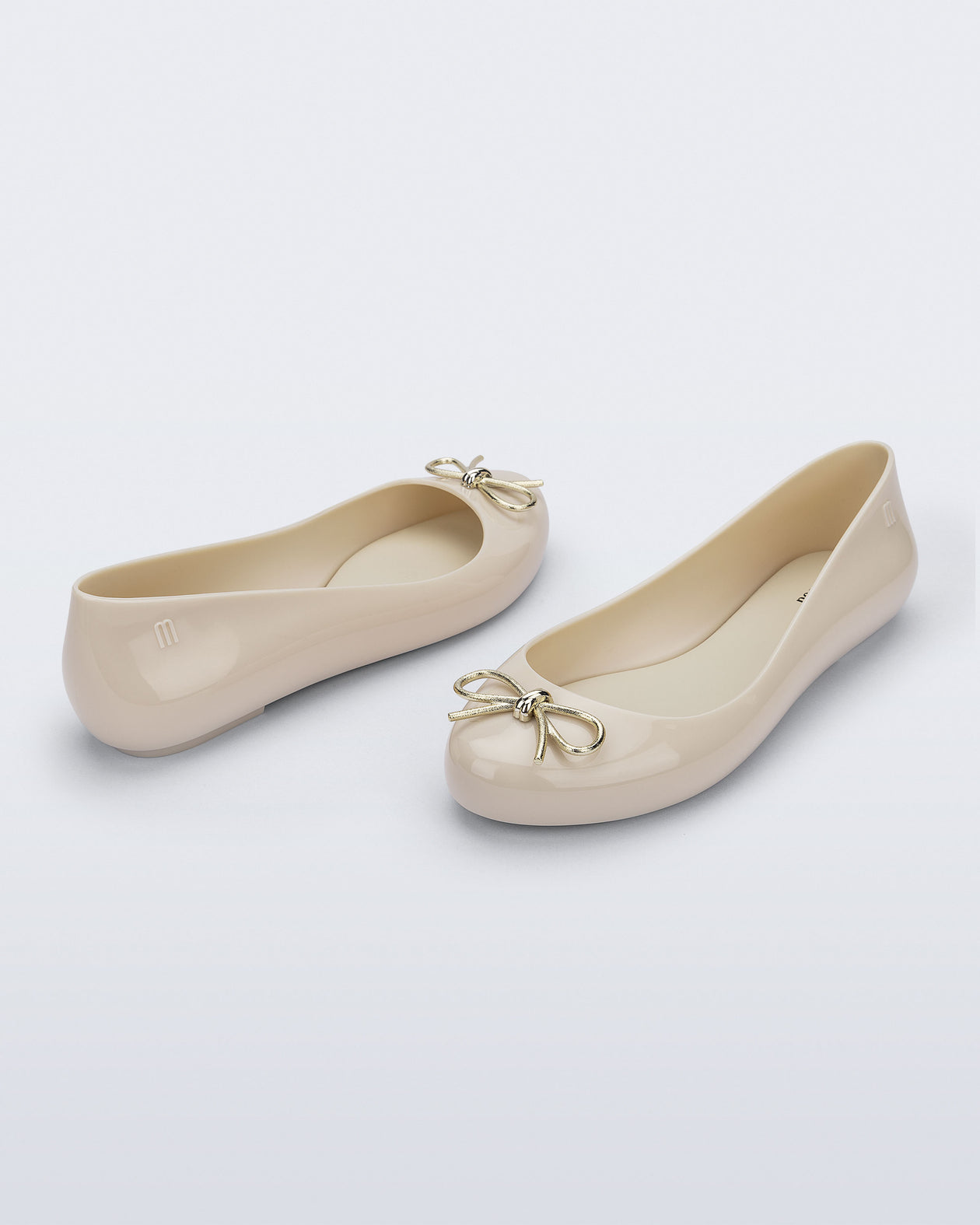 Back and angled view of a pair of beige Sweet Love Chrome flats with gold bow