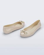 Back and angled view of a pair of beige Sweet Love Chrome flats with gold bow