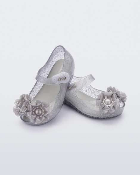 Angled view of a pair of clear grey glitter Ultragirl Springtime baby flat with grey flower and peep toe.