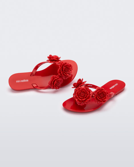 Angled view of a pair of a red Harmonic Springtime kids flip flop with three red flowers.