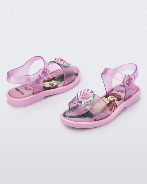 An angled front and side view of a pair of glitter pink Mini Melissa Mar Sandal Princess sandals with a seashell detail on the front strap, an ankle strap and Princess Ariel soul