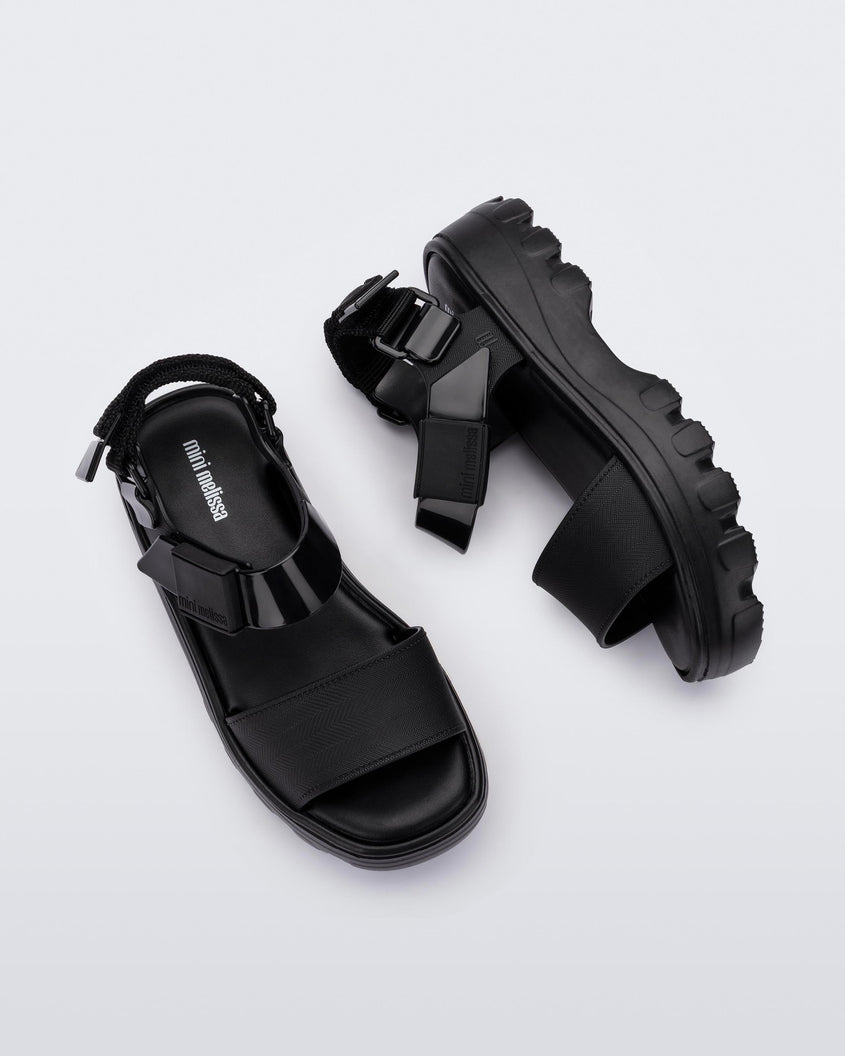 Top and side view of a pair of Mini Melissa Kick Off platform sandals in black with adjustable velcro ankle straps 