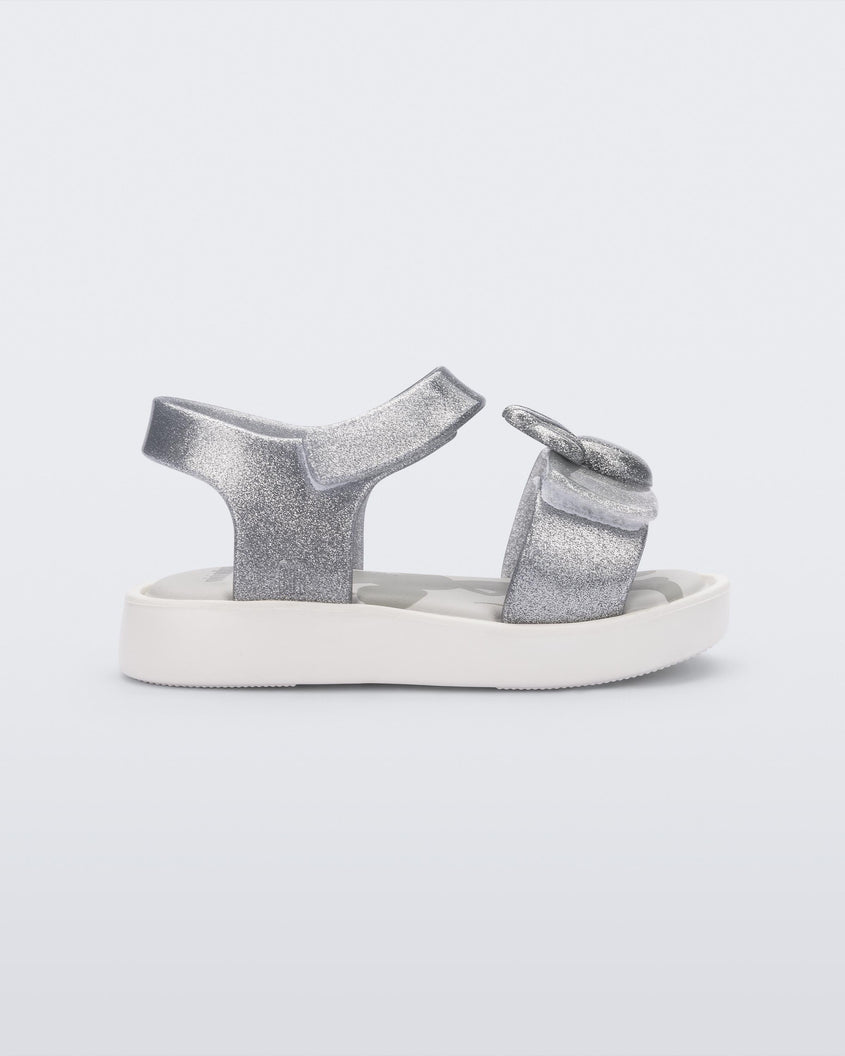 Side view of a white/glitter silver Mini Melissa Jump sandal with a Mickey Mouse logo detail on the front strap and an ankle strap