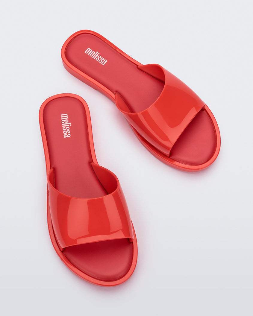 An angled top view of a pair of red tortoiseshell Melissa Miranda slides