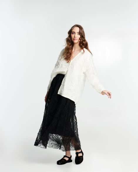 Model in a black skirt and white shirt wearing a pair of flocked black Possession Velvet fisherman sandals