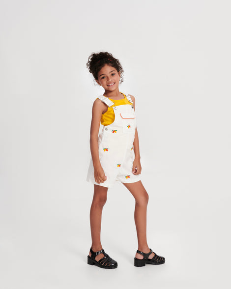 Child model in white overalls wearing a pair of pearly black Possession Heel kids fisherman sandals