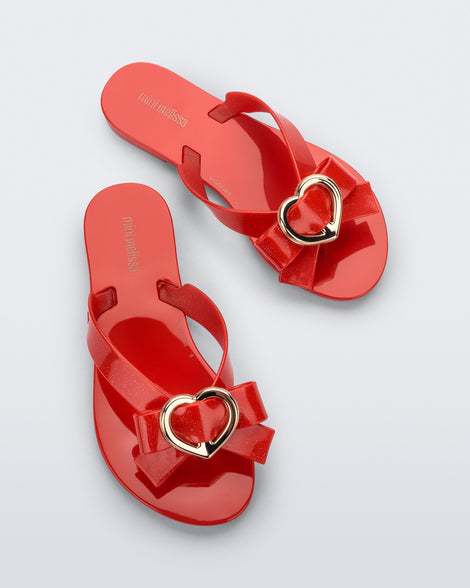 Top view of a red Mini Melissa Harmonic Heart flip flops with a red bow and gold heart detail on the straps