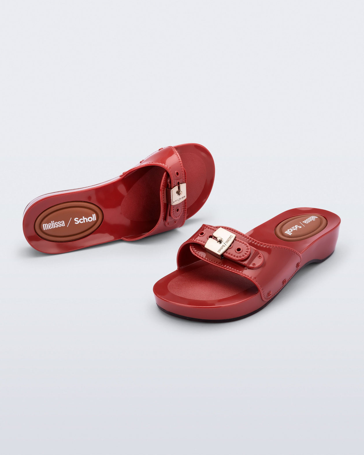 Top and angled view of a pair of red Pescura Heel + Scholl slides with top buckle