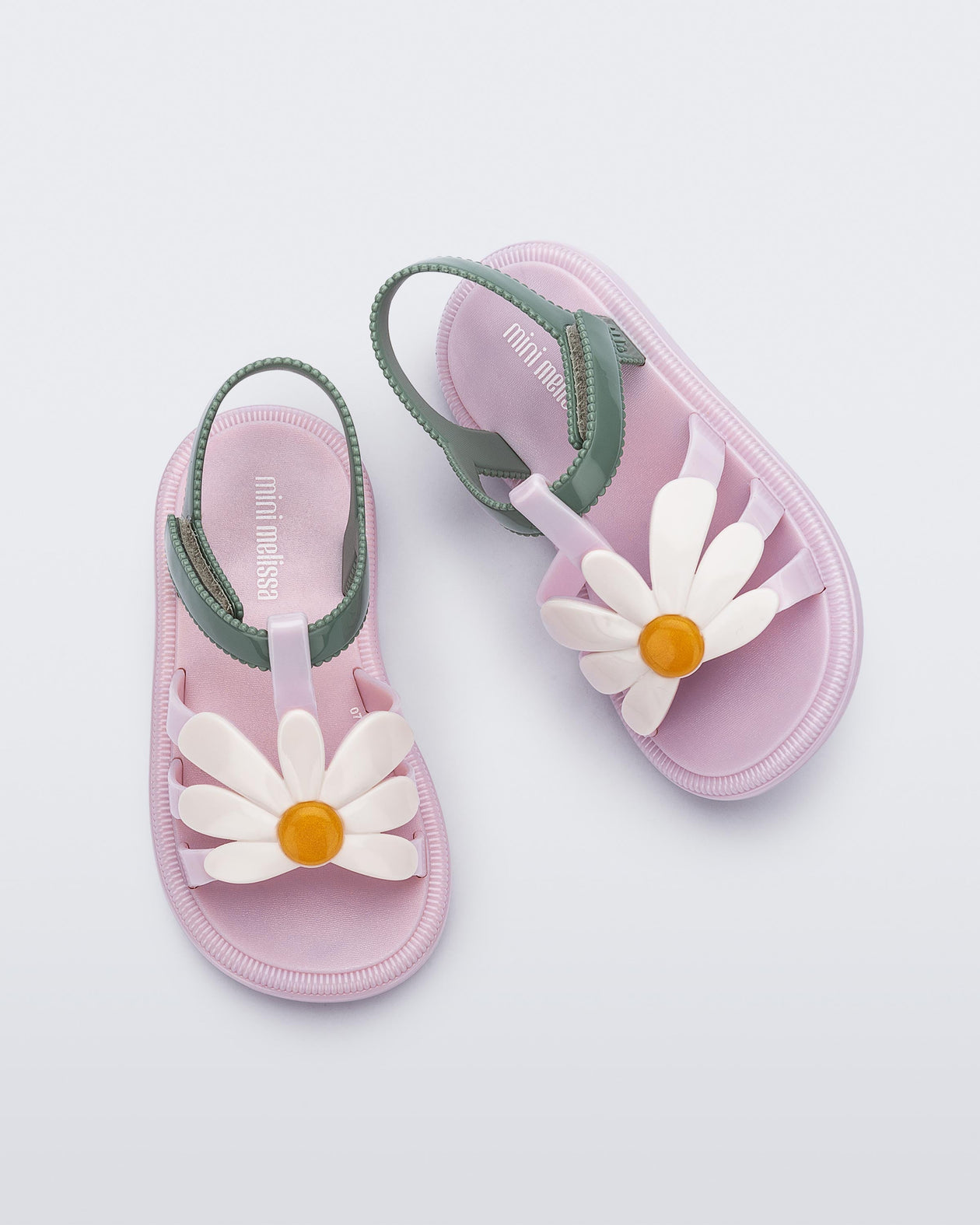 Top view of a pair of pink Hip Bloom baby sandals with white flower and green ankle strap