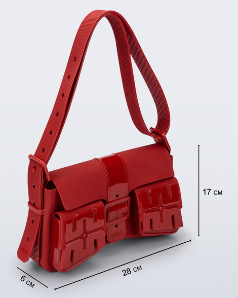 Angled view of a red Cargo bag with two small pockets on the front and an adjustable strap with measurements of the bag: 28cm x 6cm x 17cm
