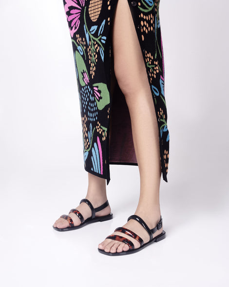Model's legs in a floral dress wearing a pair of black and tortiose Essential Wave women's sandal with adjustable buckle.