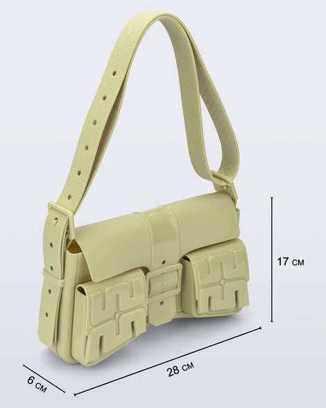 Angled view of a pastel green Cargo bag with two small pockets on the front and an adjustable strap with measurements of the bag: 28cm x 6cm x 17cm
