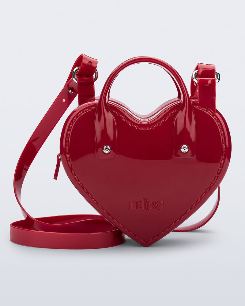 Front view of a red Heartbeat bag with small handles and longer strap.