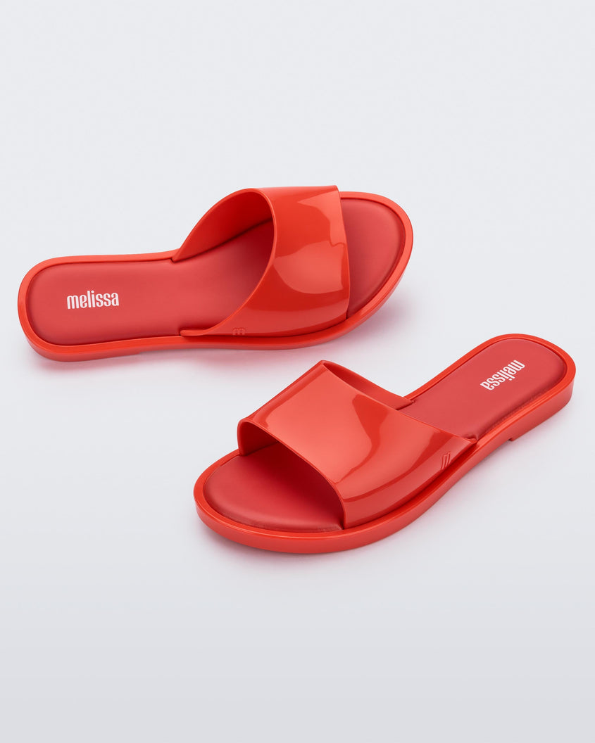 An angled side and top view of a pair of red tortoiseshell Melissa Miranda slides