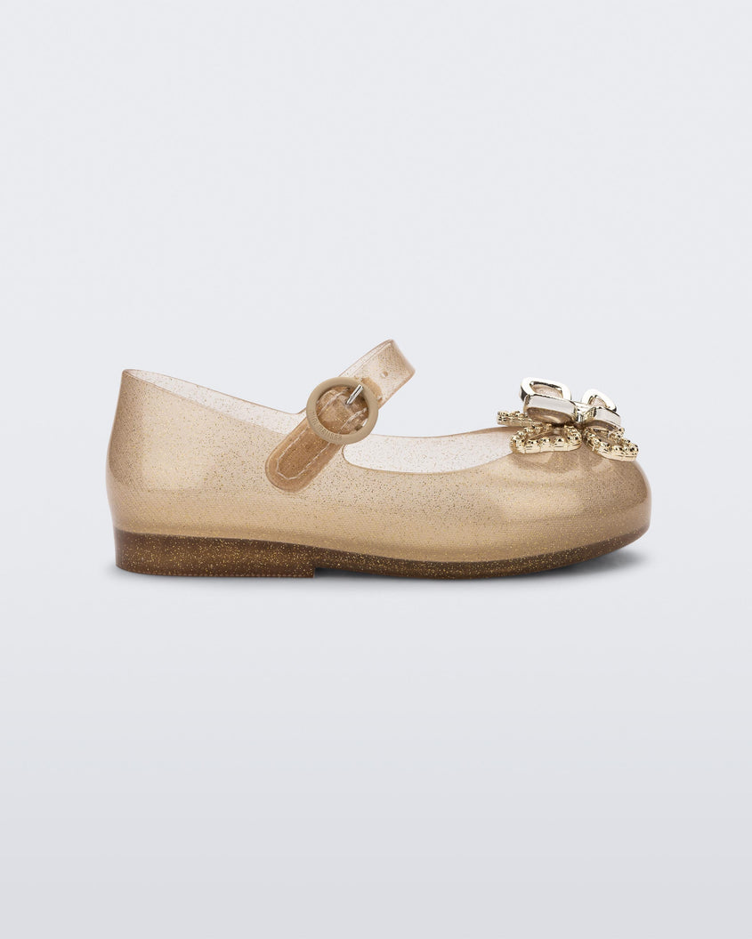 Side view of a glitter beige Mini Melissa Sweet Love Butterfly flat with a top strap and a gold butterfly detail on the toe