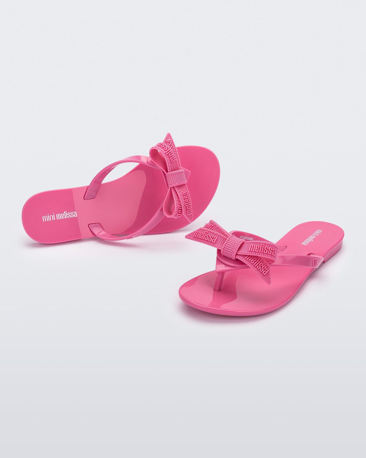 Top and angled view of a pair pink Harmonic M Lover kids flip flops with rainbow Melissa logo on bow