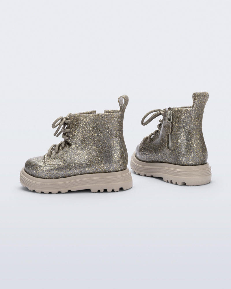 Side and back angle view of a pair of beige/golden glitter Coturno lace up baby boots