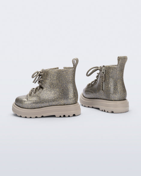 Side and back angle view of a pair of beige/golden glitter Coturno lace up baby boots