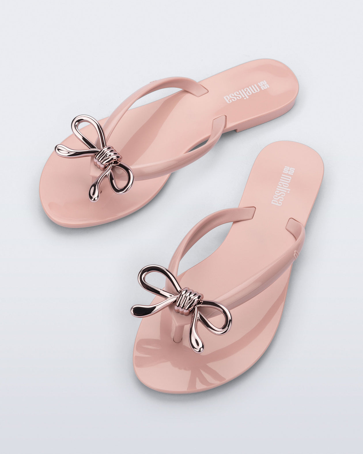 Top view of a pair of pink Harmonic Iris flip flops with rose gold bow