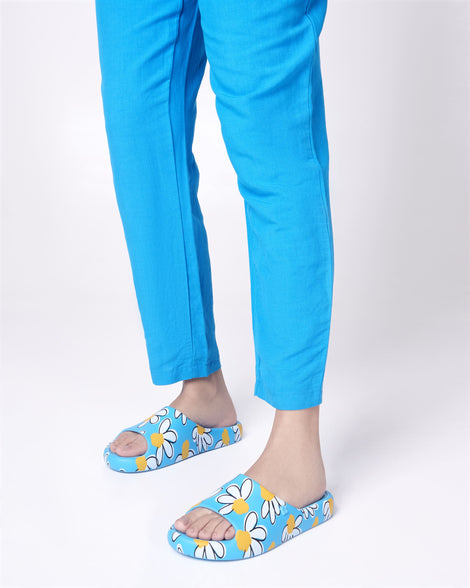 Model's legs in blue pants wearing a pair of blue Free Print Slides with daisy print flowers