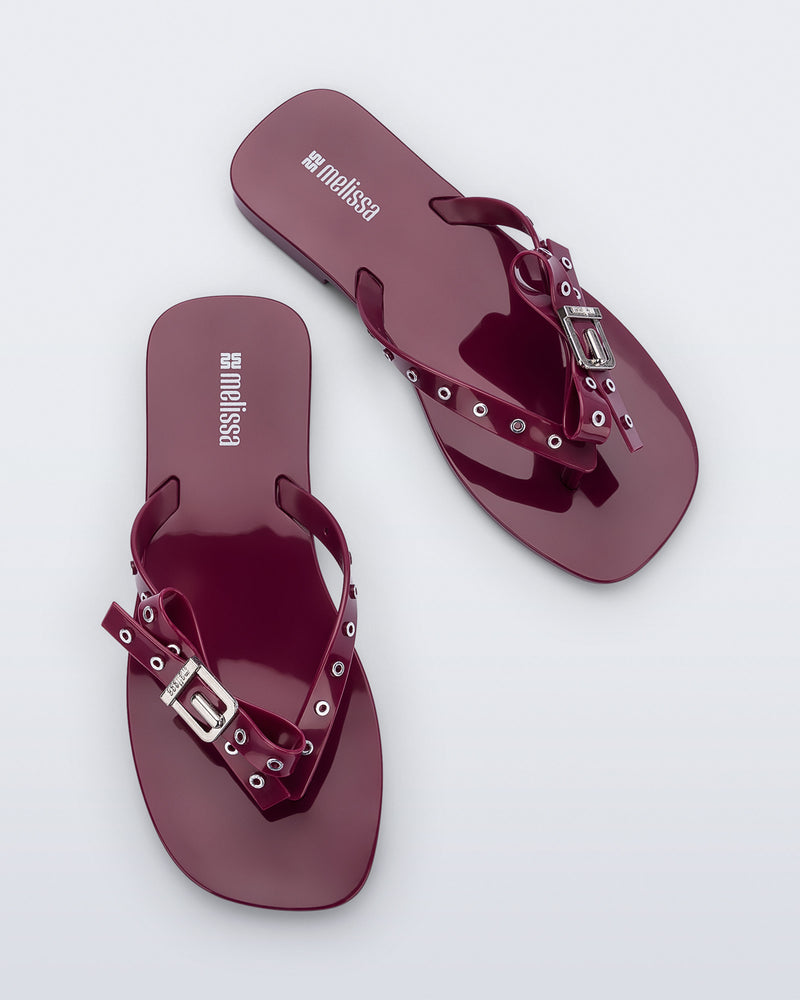 Top view of a pair of red Harmonic Squared flip flops with bow on strap