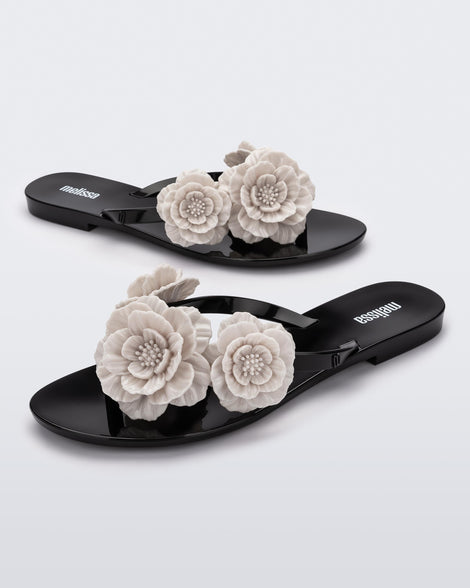 Angled view of a pair of a black Harmonic Springtime women's flip flop with 3 beige flowers