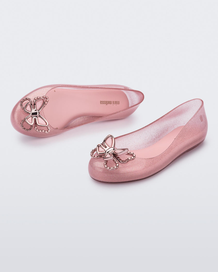 An angled front and top view of a pair of glitter pink Mini Melissa Sweet Love Butterfly flats with a pink butterfly detail on the toe