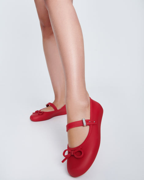 Model's legs wearing a pair of red Soft Ballerina Delicate Bow flats with top strap and bow