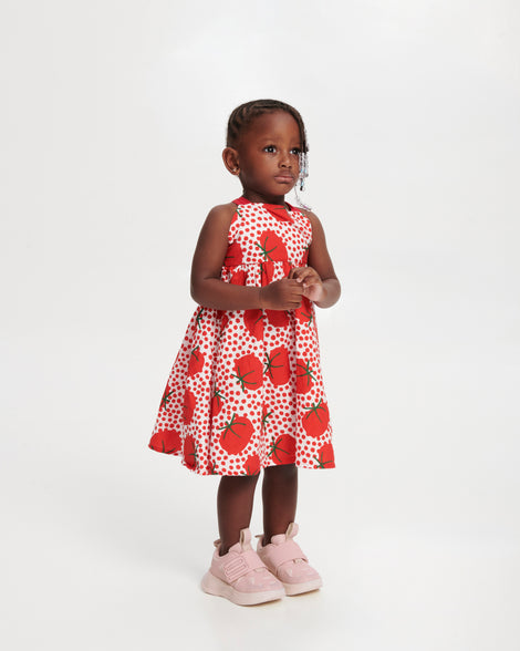 Child model in a dress with red tomatoes wearing a pair of pink X Beat baby sneakers
