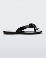 Side view of a black Mini Melissa Harmonic Heart flip flop with a black bow and gold heart detail on the straps