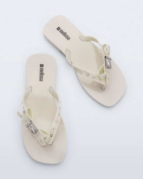 Top view of a pair of beige Harmonic Squared flip flops with bow on strap