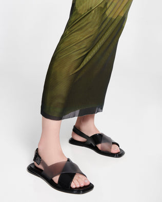 Model's legs in a green skirt wearing a pair of black Cleo sandals with back strap and crisscross top straps