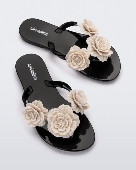 Top view of a pair of a black Harmonic Springtime kids flip flop with three  beige flowers.