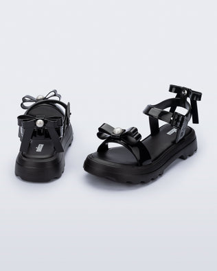 Angled and back view of a pair of black Town Bow sandals with bows and a pearl in the center of each bow