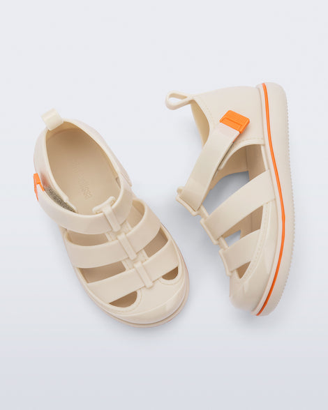 Top and side view of a pair of beige Smash closed toe baby sandals with orange trim