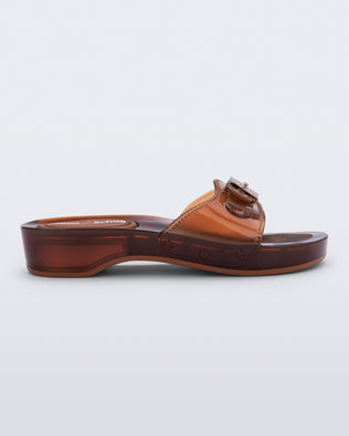Side view of a clear brown Pescura Heel + Scholl slide with top buckle