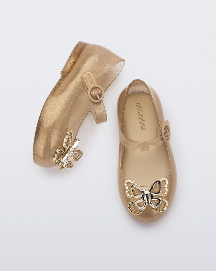 A top and side view of a pair of glitter beige Mini Melissa Sweet Love Butterfly flats with a top strap and a gold butterfly detail on the toe