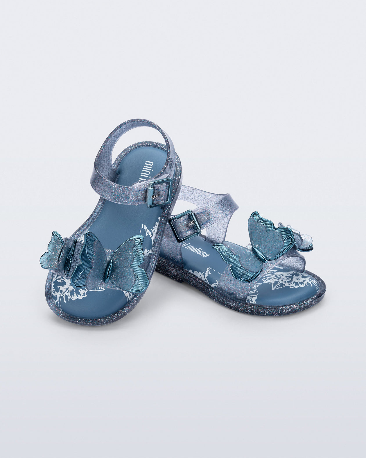 Angled view of a pair of glitter blue baby Butterfly sandals with blue butterflies